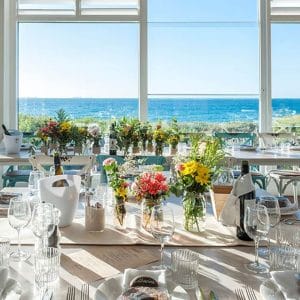 A Table Set Up With Flowers And A View Of The Ocean.