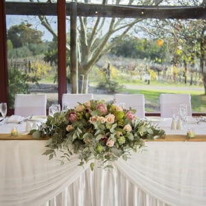 Wedding top table setting with bouquet of flowers, white seats and table decorations overlooking winery