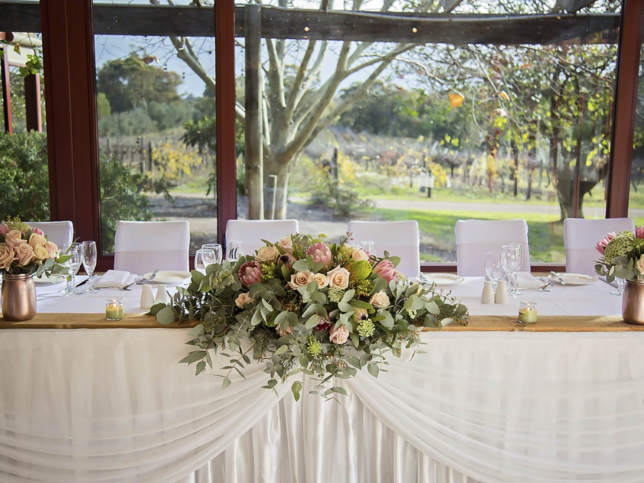 Wedding top table setting with bouquet of flowers, white seats and table decorations overlooking winery