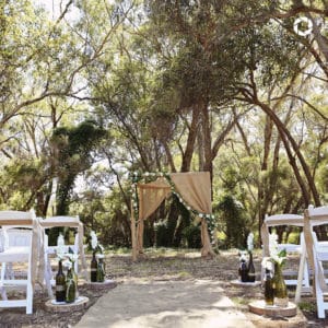 Beautifully adorned arbour with flowers and cloth surounded with white seats facing a forest backdrop