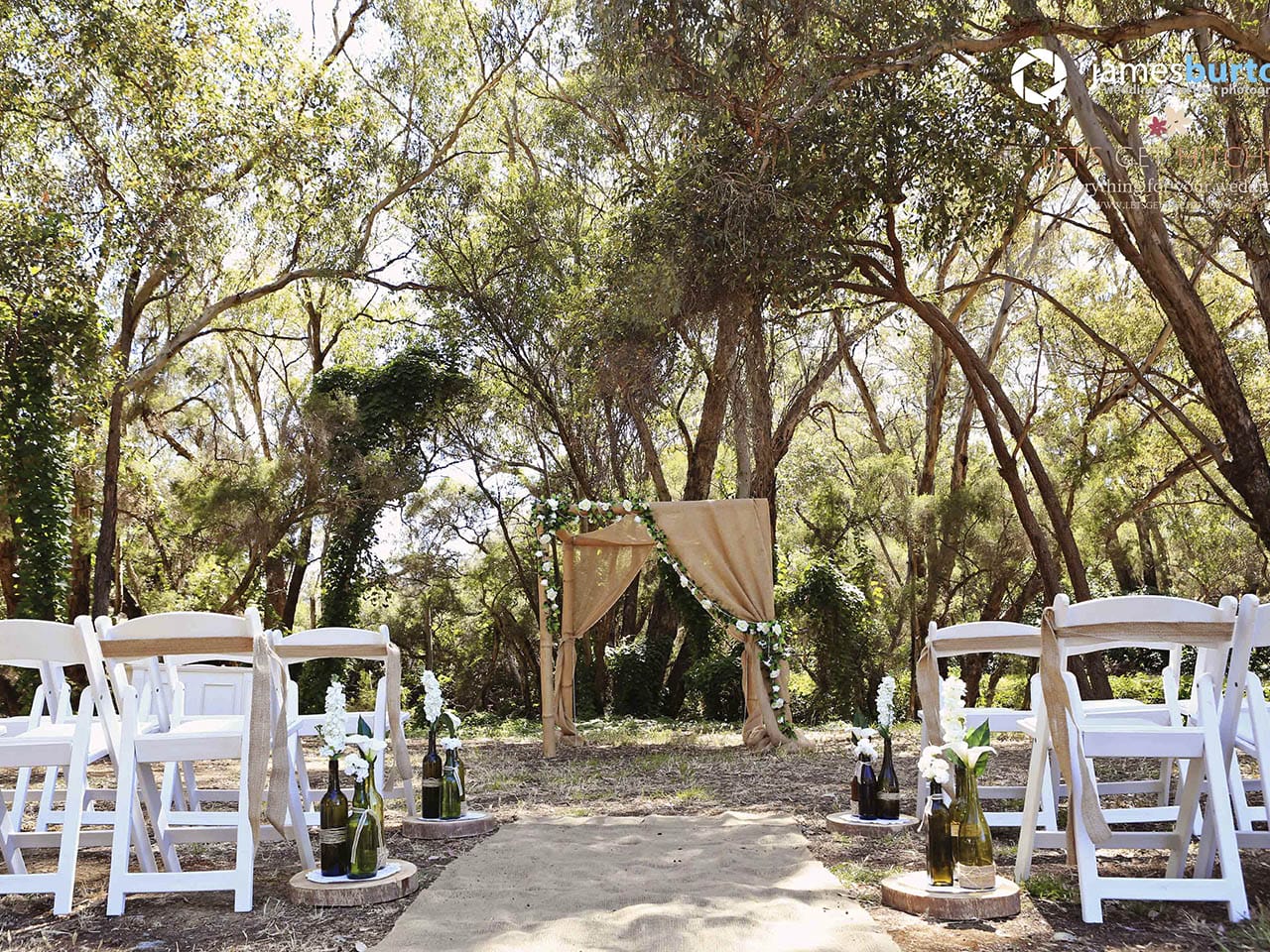 Beautifully adorned arbour with flowers and cloth surounded with white seats facing a forest backdrop