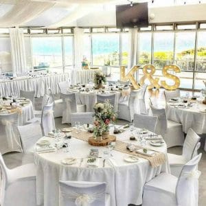 A Bright Open Room, With White Chairs And Round Tables With A Ocean View.
