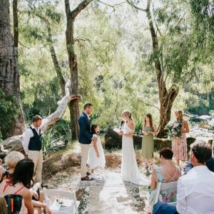 Wedding Ceremony Taking Place Next To A River In A Forest Area.