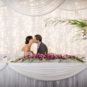 A Wedding Table With The Groom And Bride Sitting And Kissing.