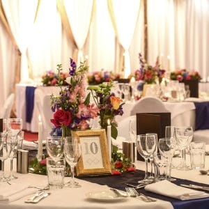 Flower Centerpieces With Table Number, Wine Glasses, Table Napkins, Spoon And Forks And Stage Behind
