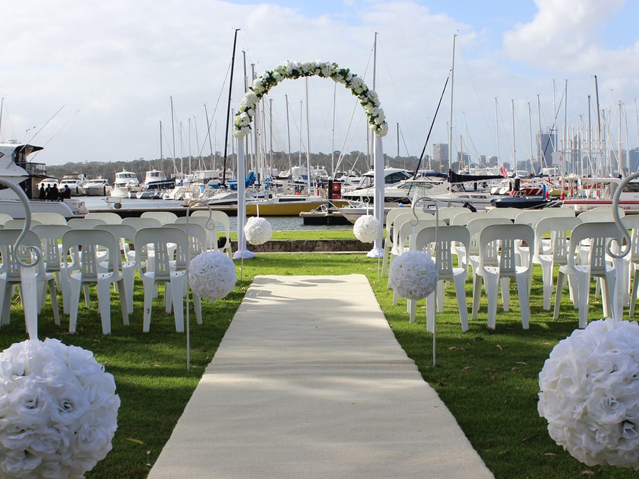 Wedding Ceremony Setup Near The Sea With White Carpet, Flowers, Flower Arc And Boats Behind