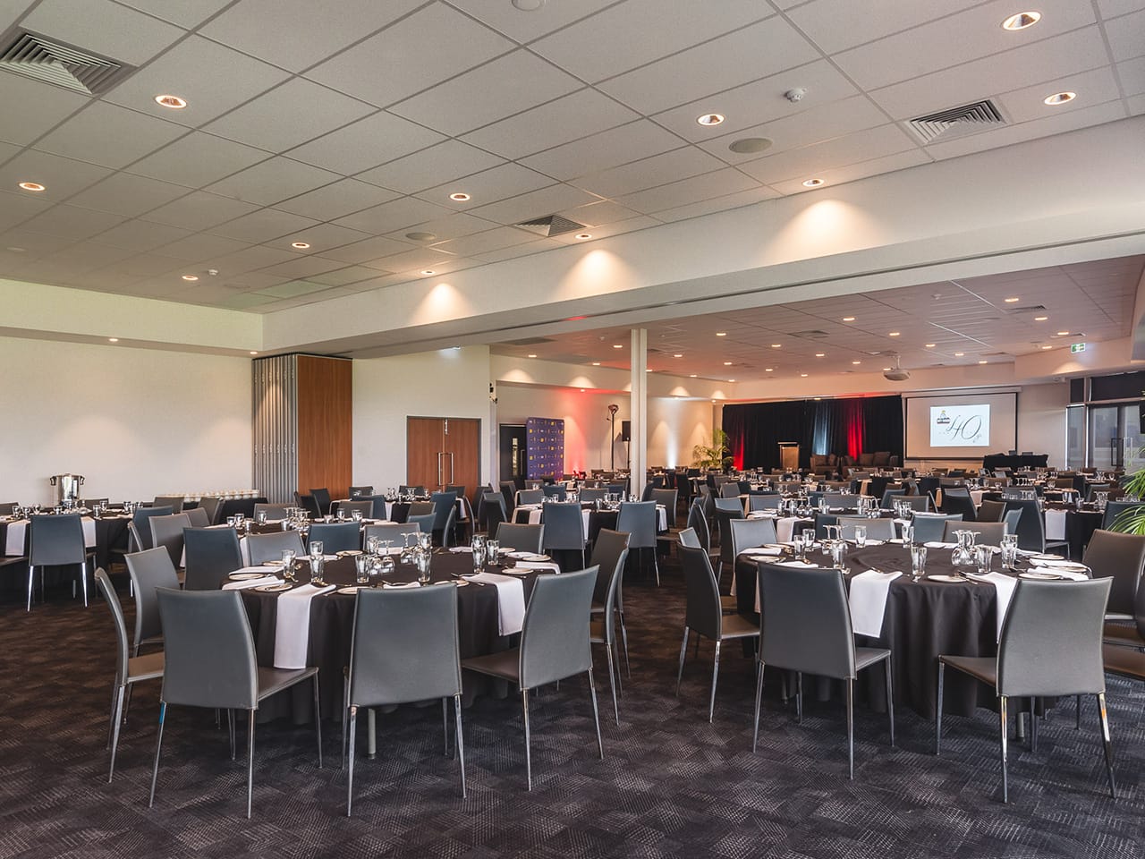 Tables And Chairs In Banquet Style Setup Inside The Function Room With Projection Screen In Front