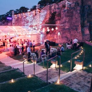 People Gathering Outside The Function Room In The Evening With Cocktail Tables And Round Hanging Lights