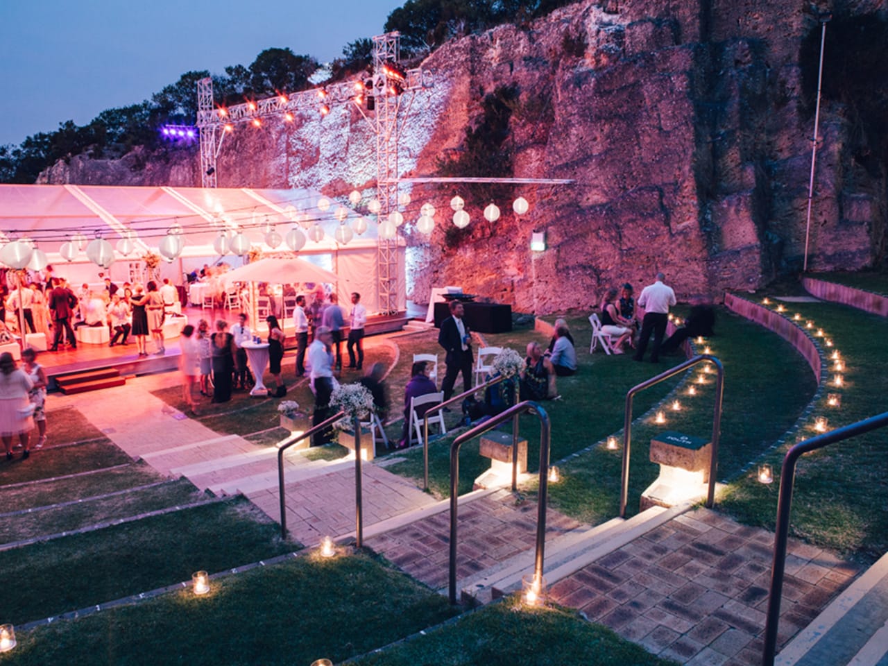 People Gathering Outside The Function Room In The Evening With Cocktail Tables And Round Hanging Lights
