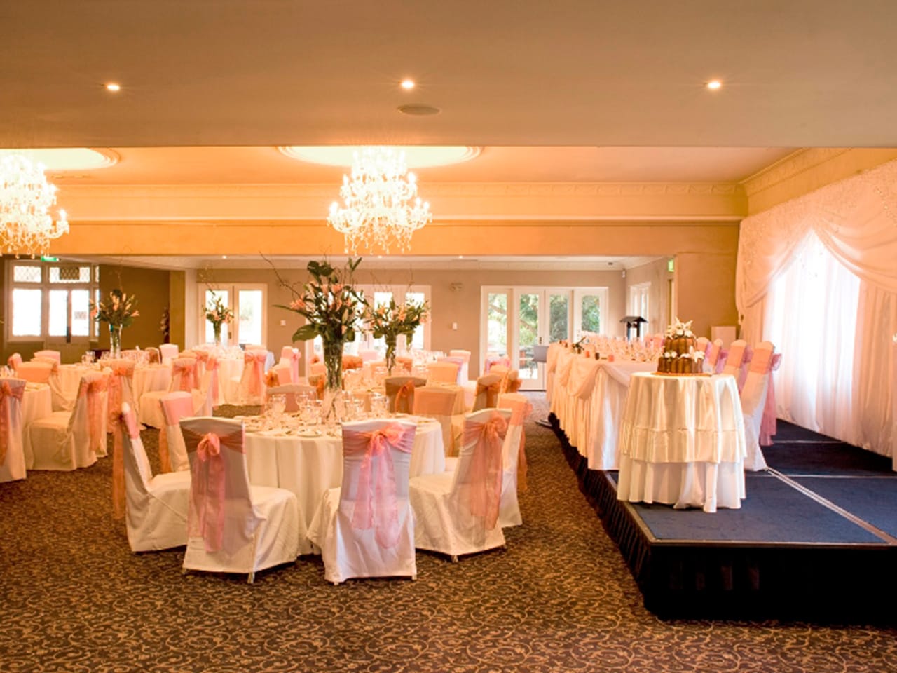 Long Table, Cake Table On Stage And Banquet Style Setup Inside The Function Room With Chandeliers