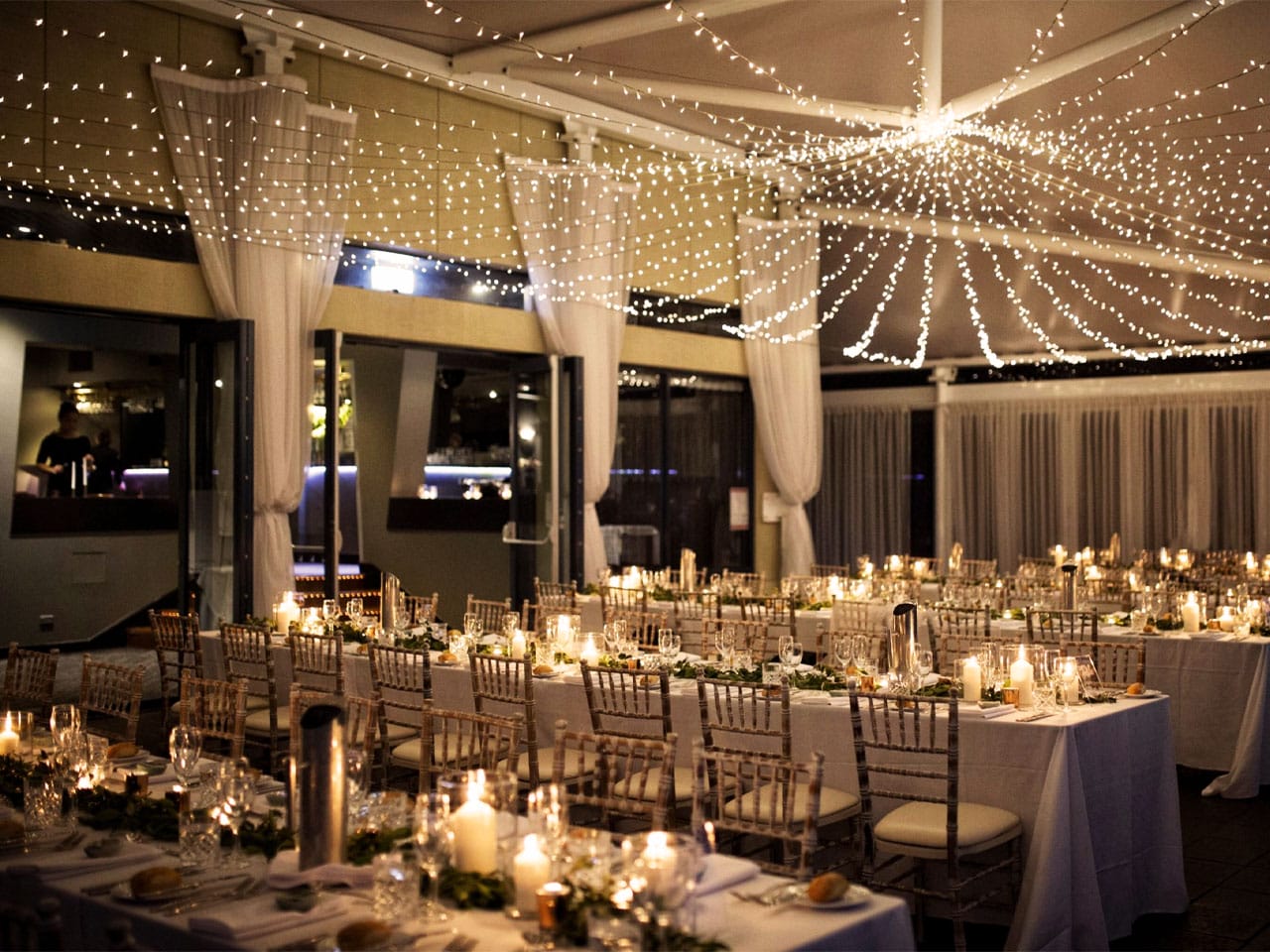 Long Tables With Chairs And String Lights Inside The Function Room
