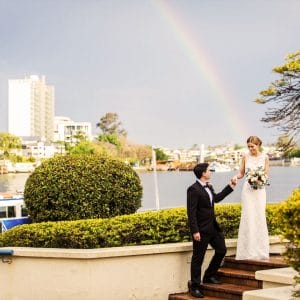 Groom assisting bride down stairs overlooking Brisbane river