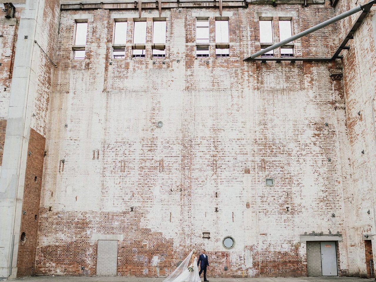 Wedding couple walking past huge white wall