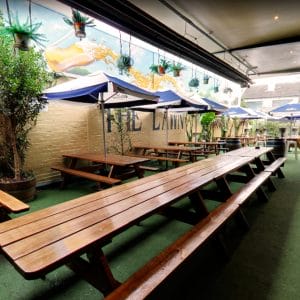 Wooden Tables And Chairs With Umbrellas And Green Plants In The Outdoor Function Venue
