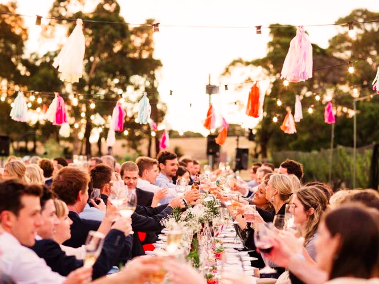 Guests Wine Toasting In A Long Table Under The Sky