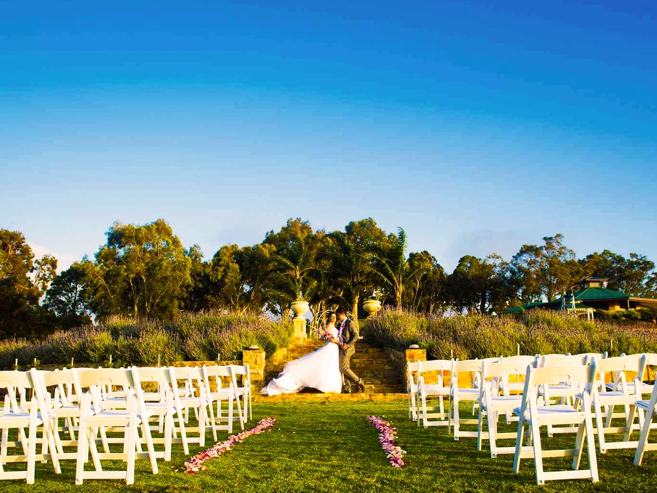 Bride And Groom Taking Photo With White Chairs In Front Of Them