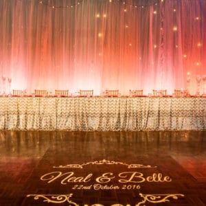 A Long Table With Chairs, Pink Colored Backdrop With String Lights And A Dance Stage In Front