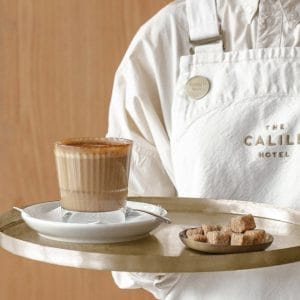 Full cup of coffee with sugar cube bowl on a tray carried by waiter