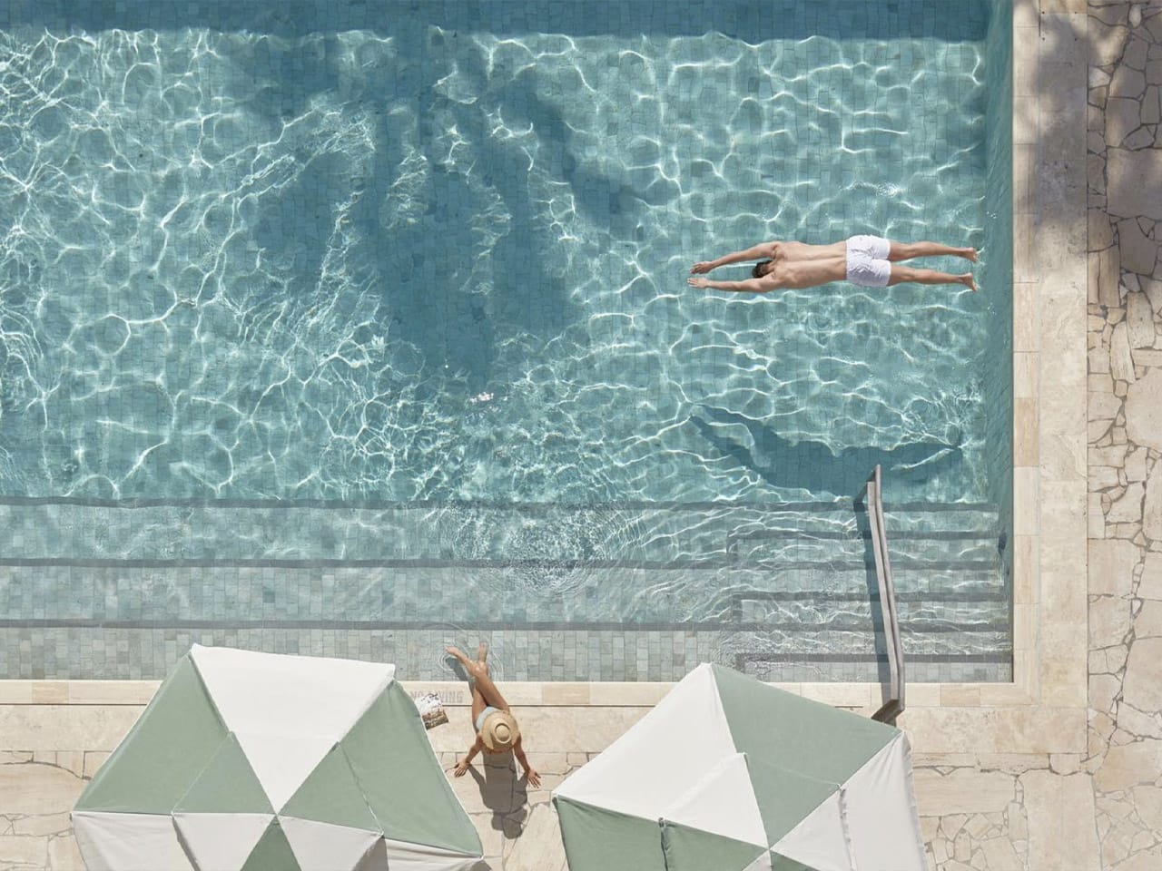 Overhead view of pool with male diving in and female sitting on side