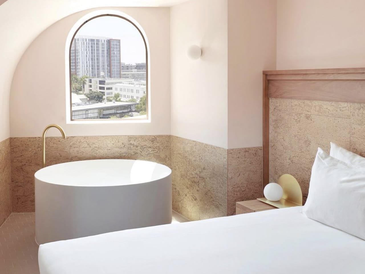 Hotel bedroom with round bath and arched window overlooking Brisbane