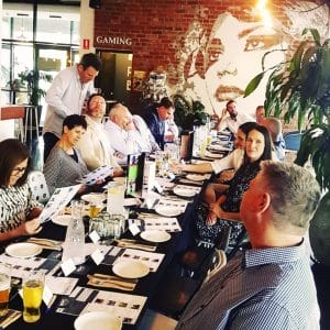 Lunch guests enjoying food at long table in front of brick wall with mural