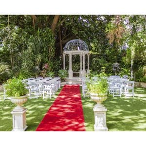 Garden gazebo set for a wedding with red carpet and rows of white chairs either side
