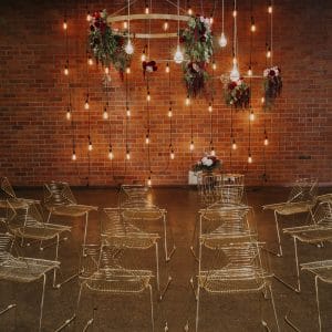 Brick wall decorated with lights with empty wire chairs ready for ceremony