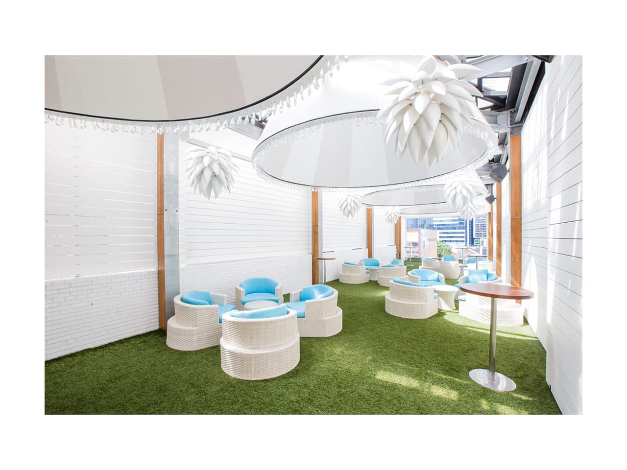 Semi-outdoor function room with white decor and blue and white individual seating with round tables and large overhead lighting
