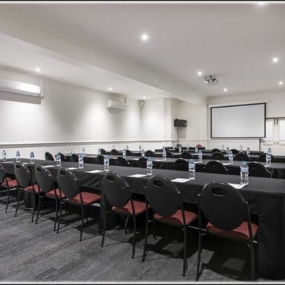 Large conference room with rows of seats and black tables with projector screen