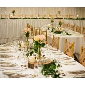 Room set for wedding reception with white and pink tables and wooden chairs