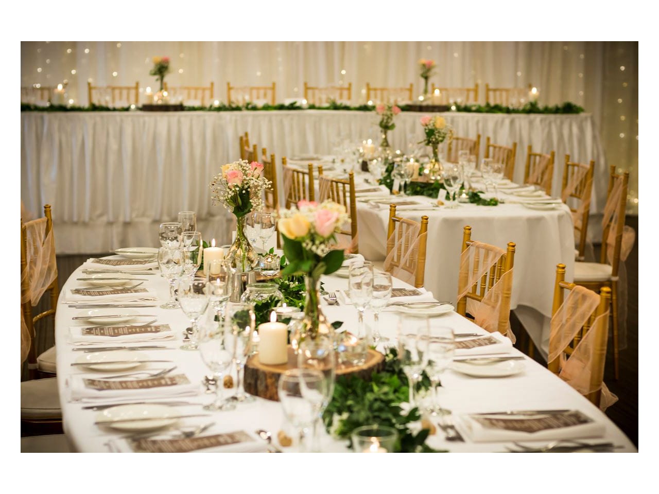 Room set for wedding reception with white and pink tables and wooden chairs