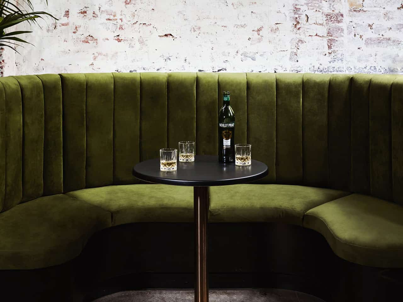 Green sofa with round table and whiskey bottle against brick white washed wall
